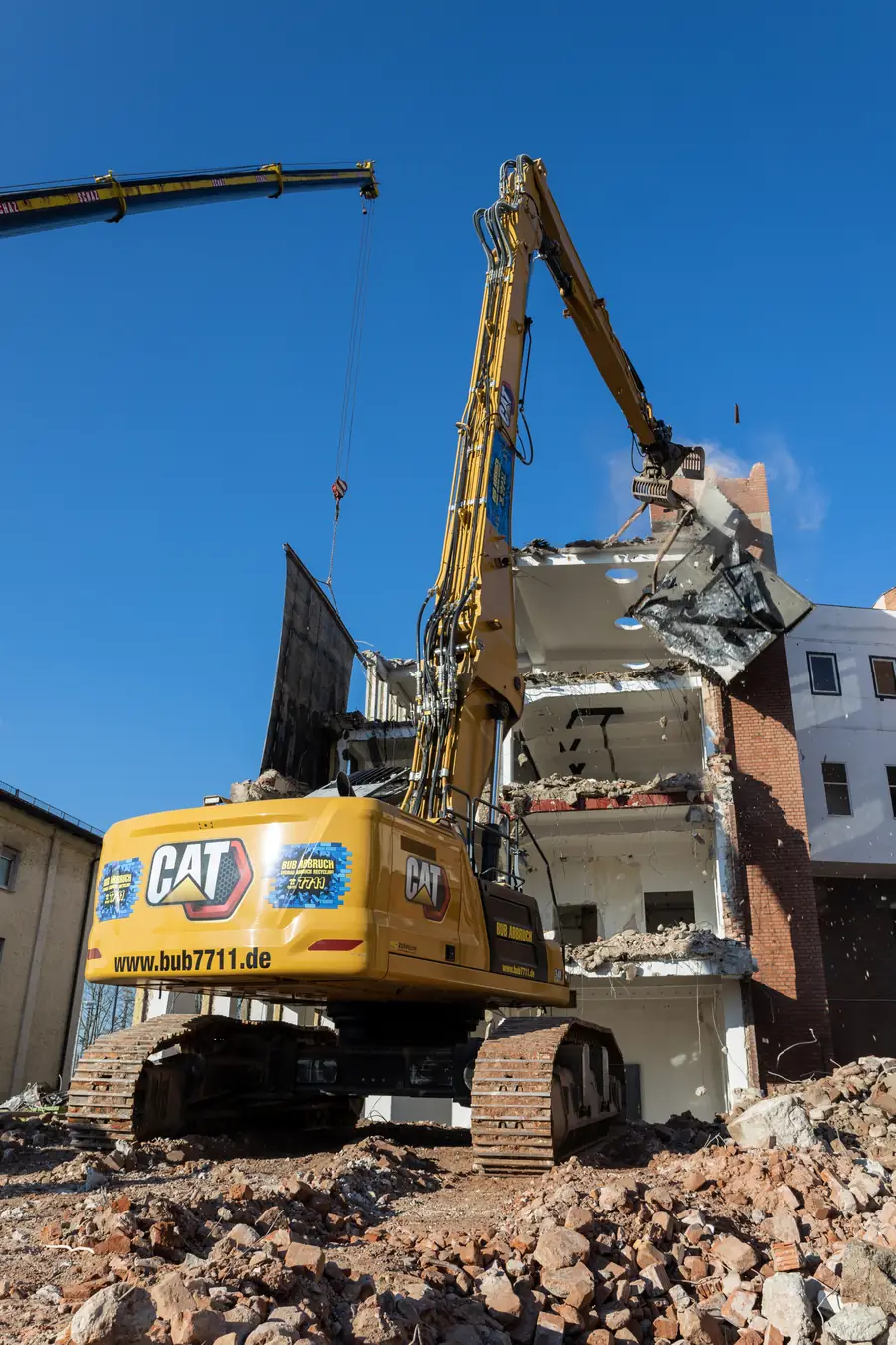 Longfrontbagger CAT 340NG UHD von Bub mit ausgefahrenem Abbruchausleger vor einem Gebäuderest